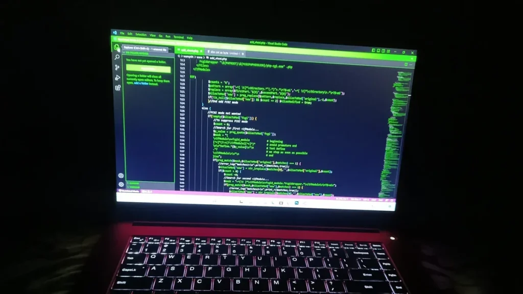 A laptop with a glowing keyboard and an open code editor in a dark room