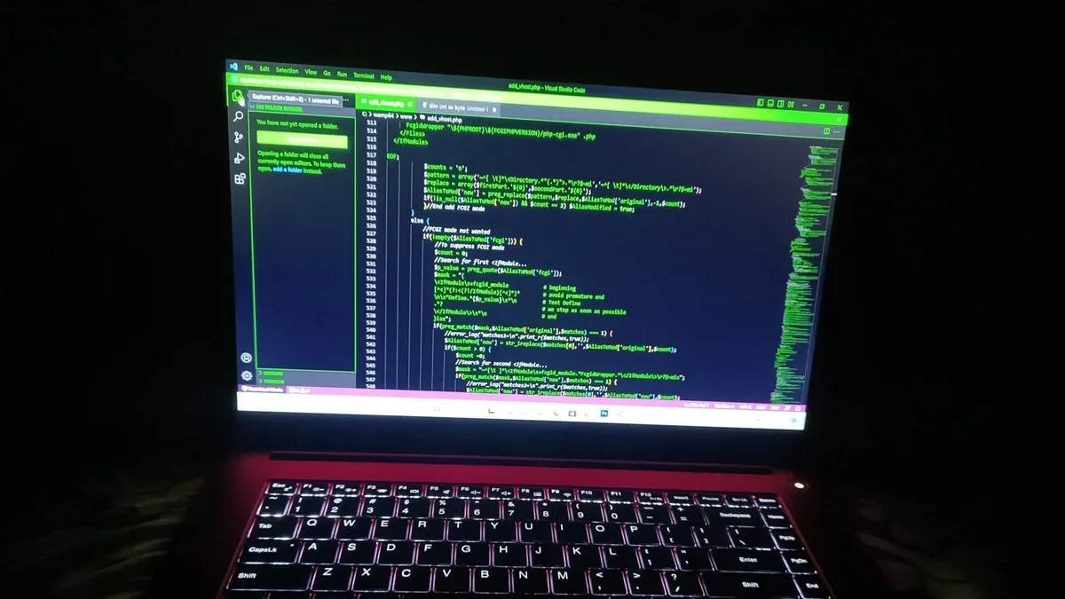 A laptop with a glowing keyboard and an open code editor in a dark room