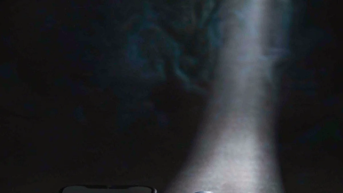 A small charm device and a phone on a dark surface with soft light