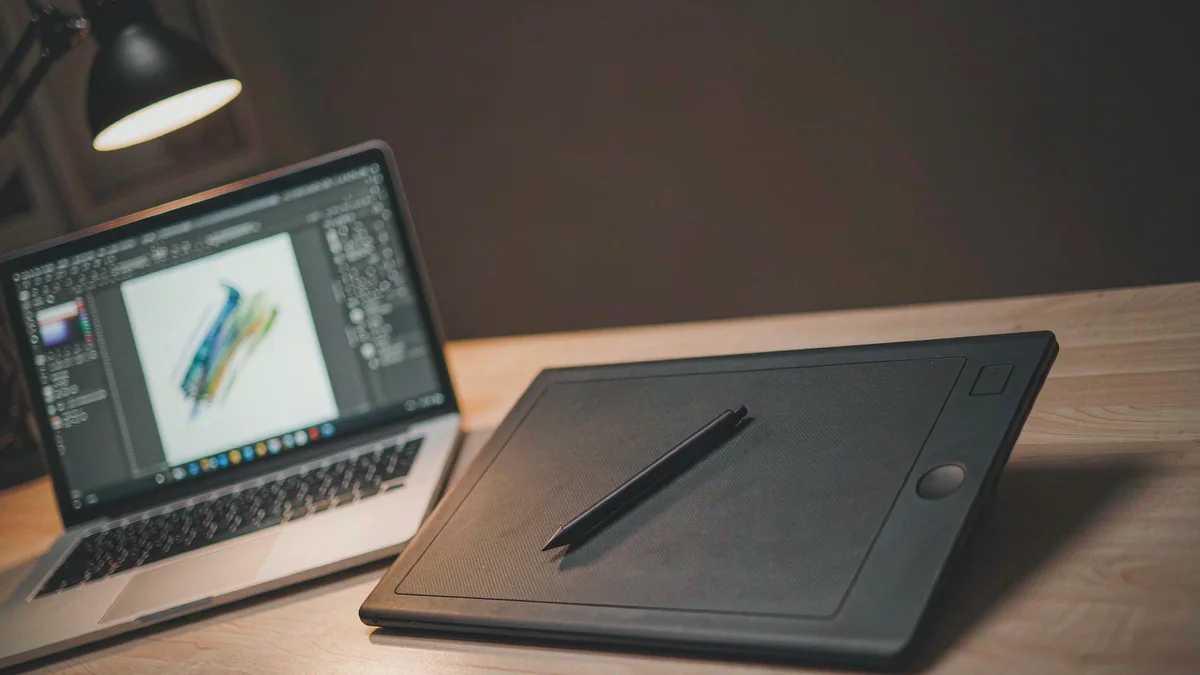 A drawing tablet with a stylus beside a laptop showing a painting app