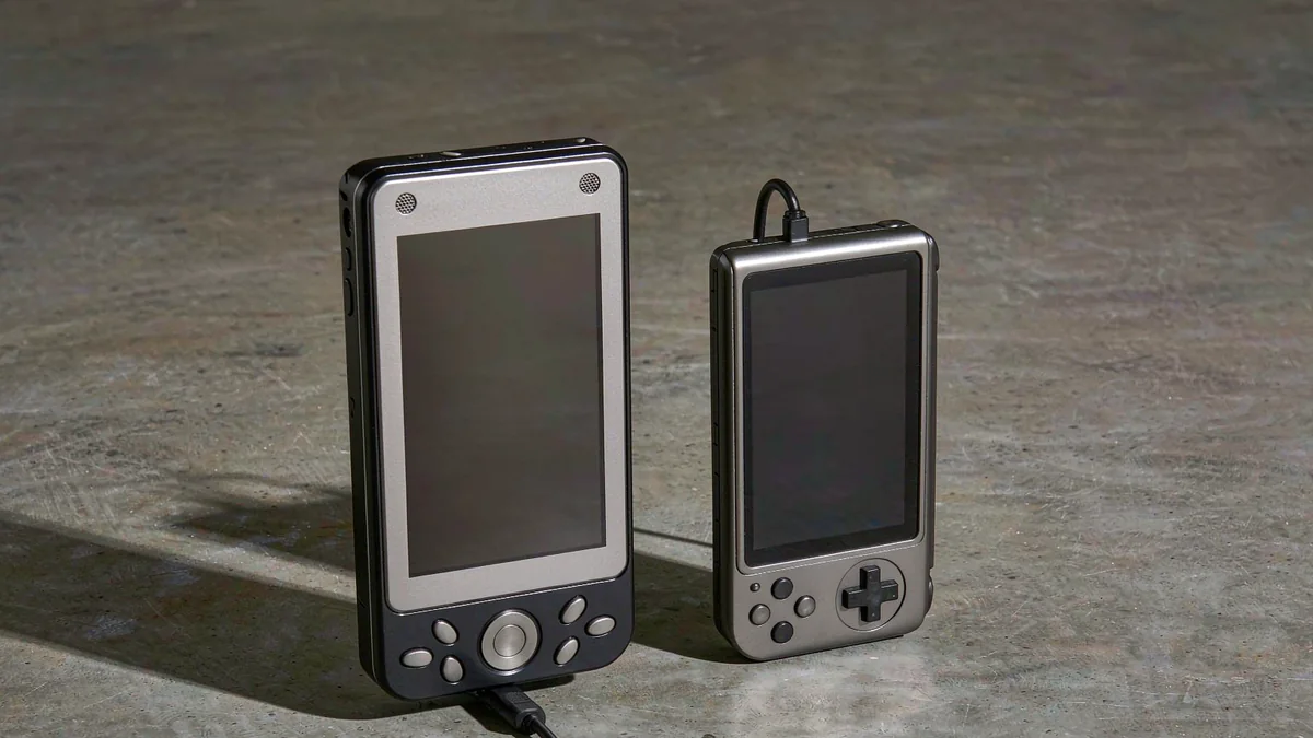 Two handheld game consoles standing side by side on a concrete surface