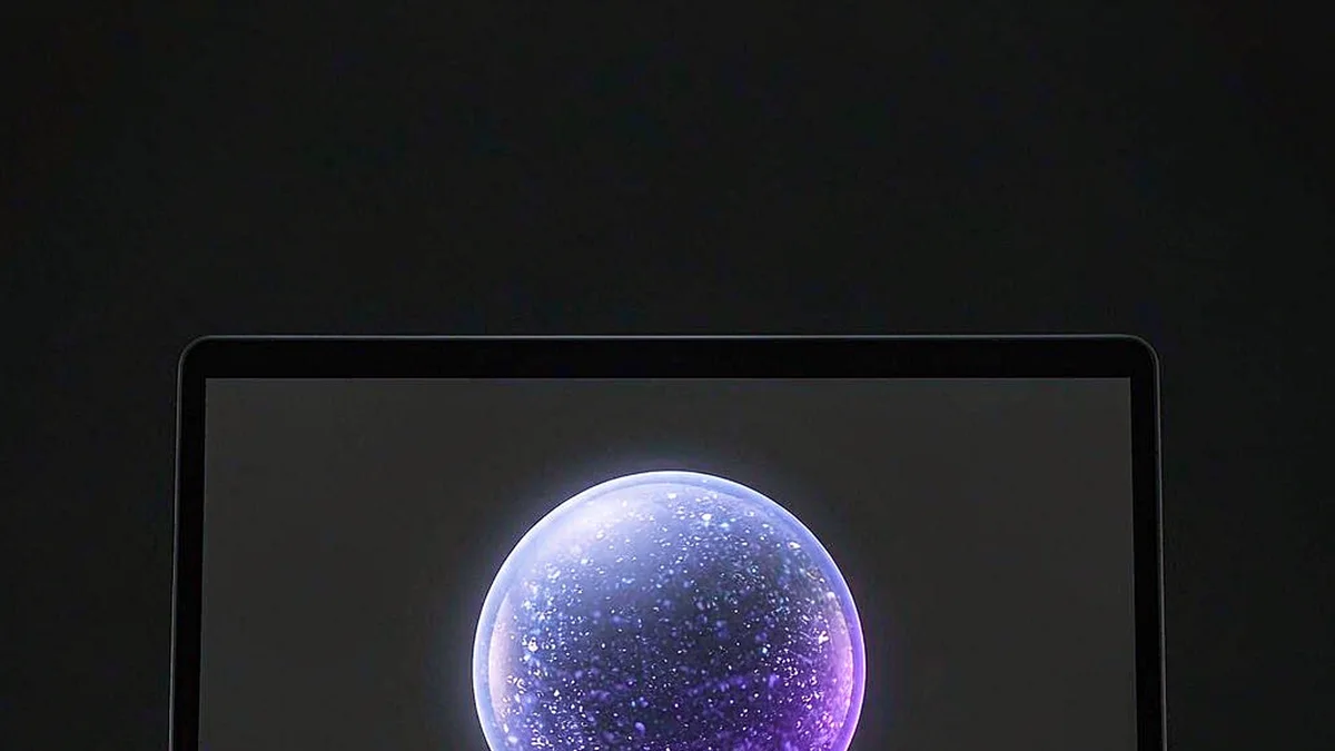 A glowing sphere of light above an open laptop on a dark desk